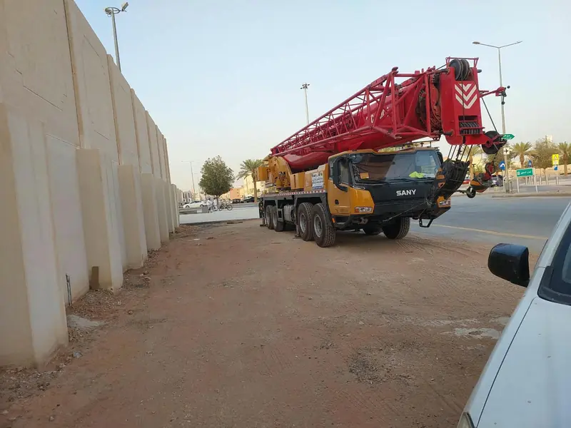 كرين متنقل بذراع أحمر متوقف بجانب طريق استعدادًا لأعمال الرفع